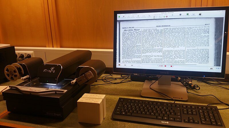 Mikrofilmlesegerät, eine Art kleiner Scanner, daneben ein Bildschirm mit einem vergrößerten Zeitungsartikel